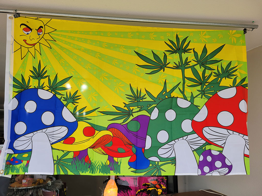 flag with graphic of sun shining on marijuana leaves and colorful mushrooms